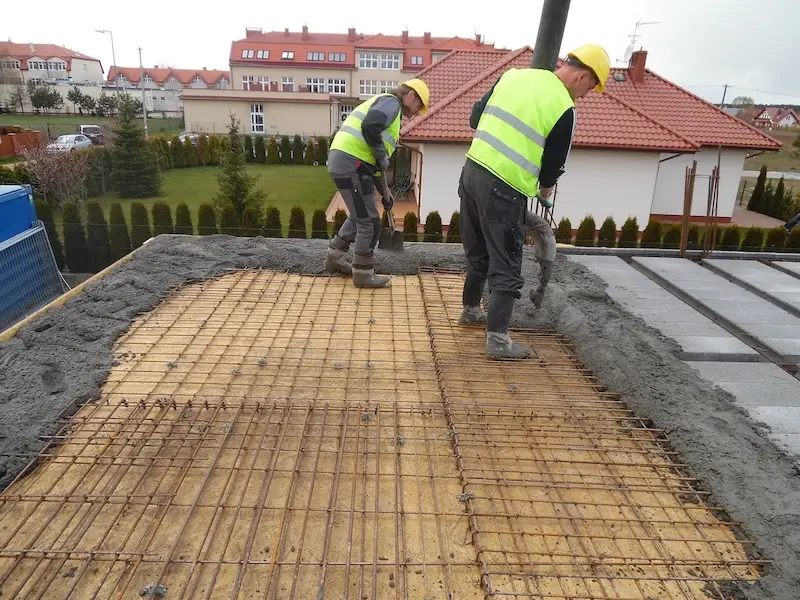 Budowa domu jednorodzinnego – rozprowadzanie betonu po zbrojeniu stropu przez pracownika