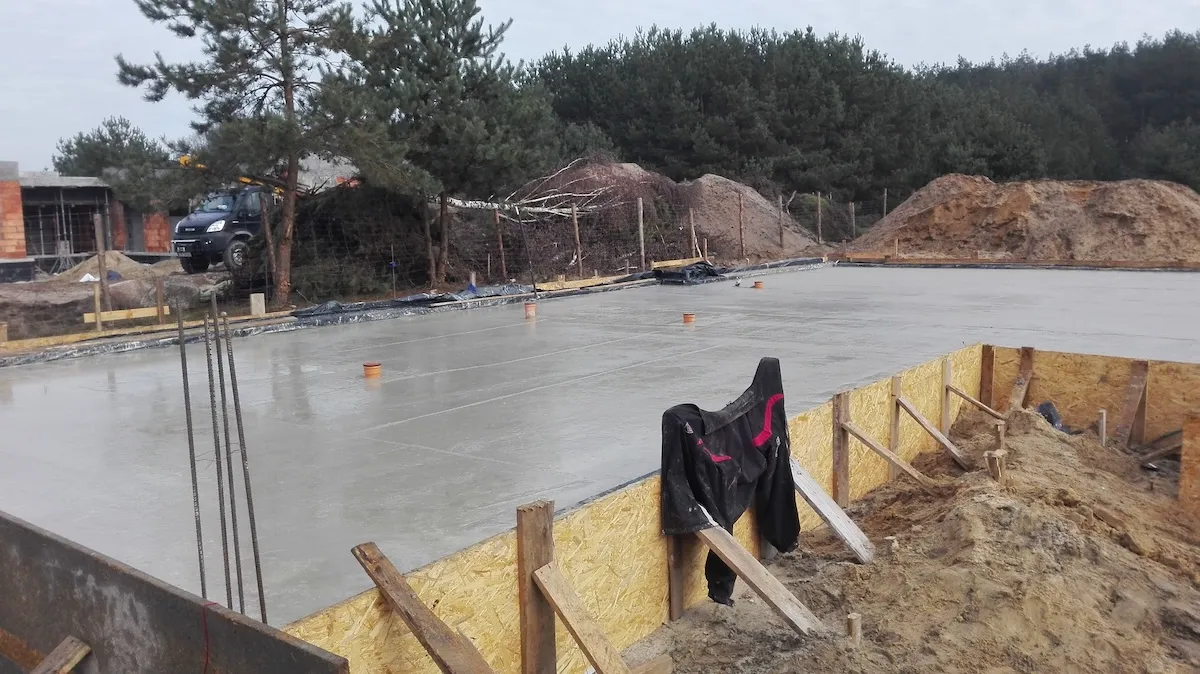 Budowa domu jednorodzinnego – prace przy krawędzi płyty fundamentowej na tle lasu